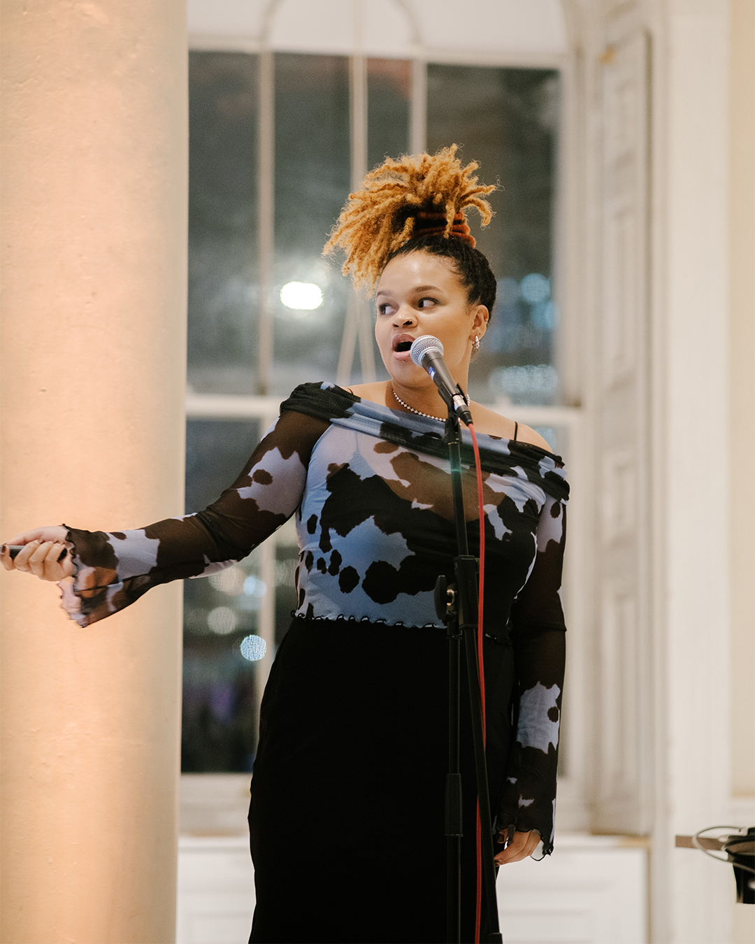 Abigail Sol, a Black woman, presents to a crowd of people. She is stood in front of a microphone talking.