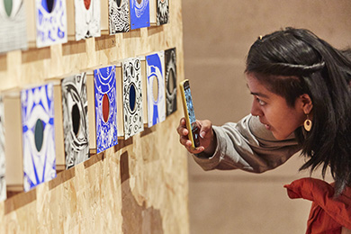 A young person takes a mobile phone photo of an artwork at the National Saturday Club Summer Show in 2022